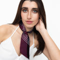 Model trägt ein schmales Seidentuch (Twilly) in zwei leichten unterschiedlichen Bordeaux - tönen, mit weißen Linien strukturiert, um den Hals geknotet.
