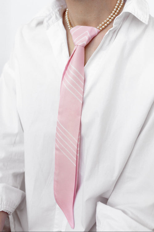 Model trägt einen rosafarbenen Seidentwilly mit einer Perlenkette als Krawatte gebunden.