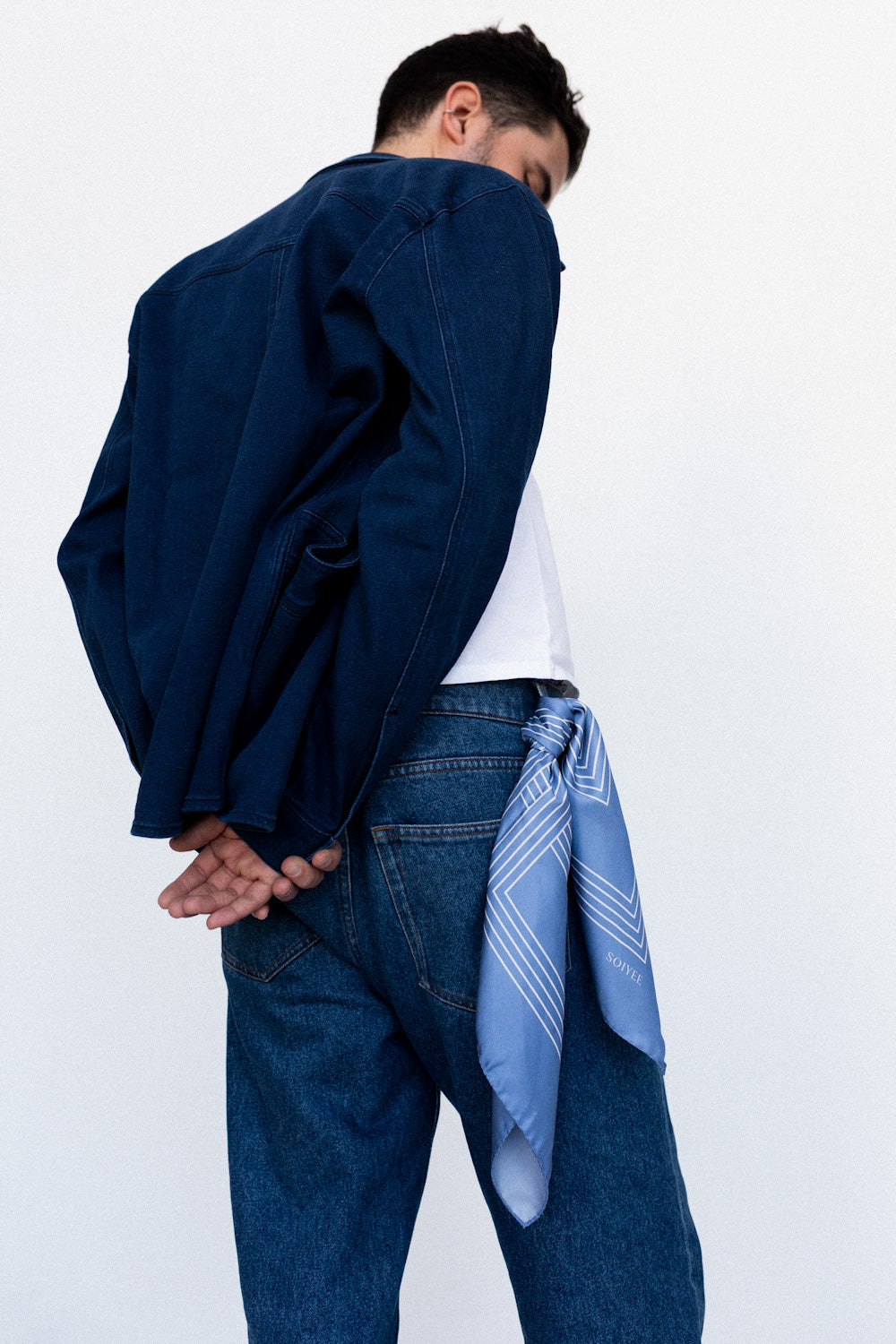 Männliches Model trägt ein blaues Seidentuch mit weißem Quadratmuster an der Jeanshose gebunden.