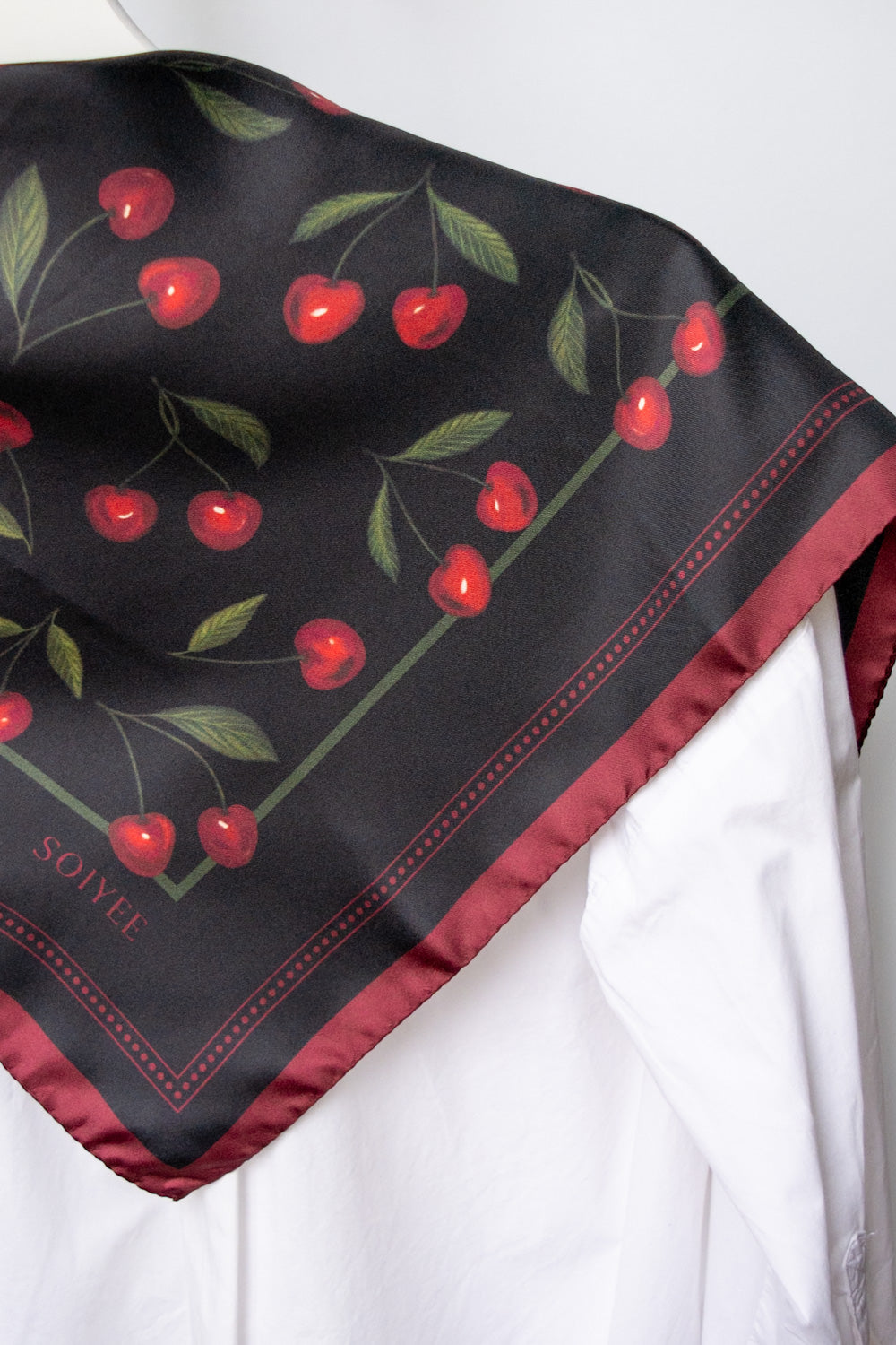 Schwarzes Seidentuch mit Kirschprint über einer weißen Bluse.