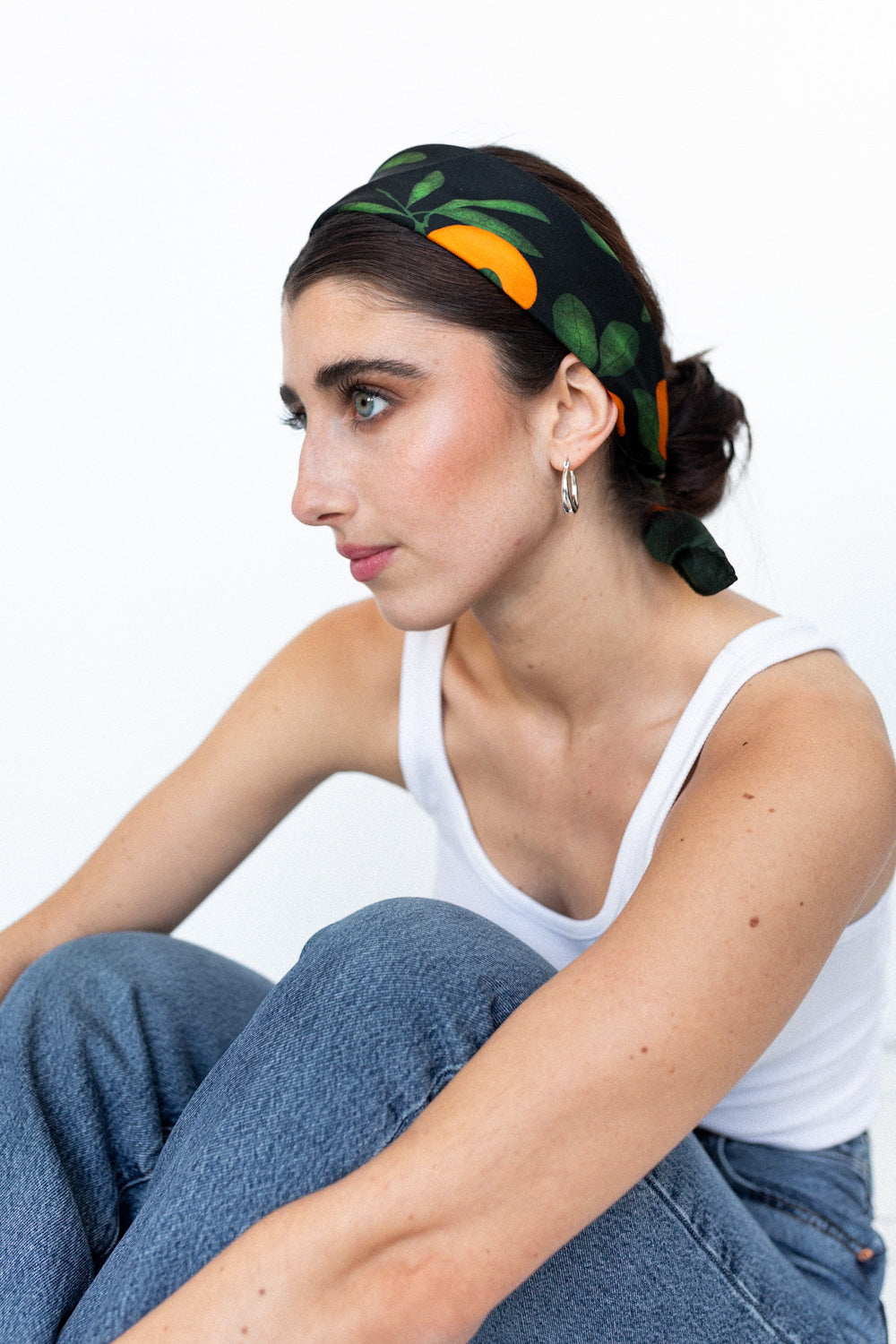 Model trägt ein schwarzes Seidentuch mit Orangenprint als Haarband gebunden.