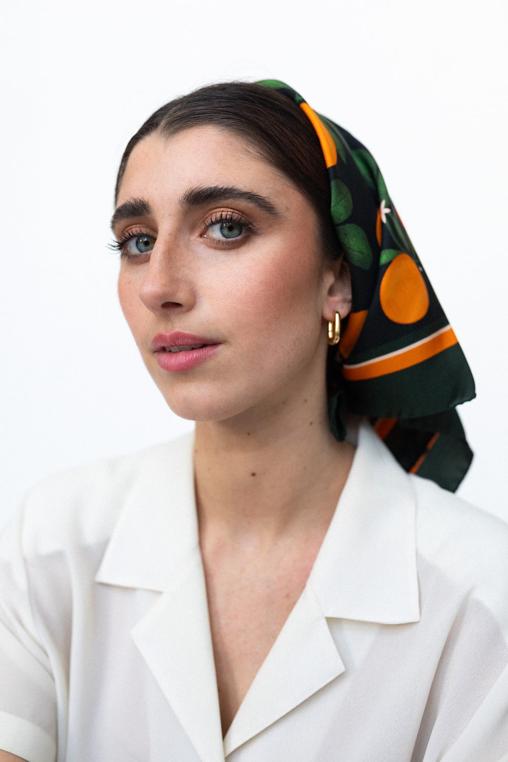 Model trägt ein schwarzes Seidentuch mit Orangenprint als Kopftuch gebunden.